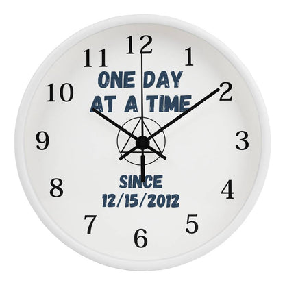 White wall clock close-up with black hands, blue “ONE DAY AT A TIME” and “SINCE 12/15/2012”