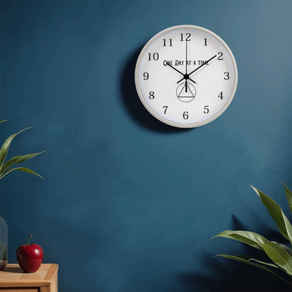 White round wall clock with “One Day At A Time” text, black hour markers, and hanging icon