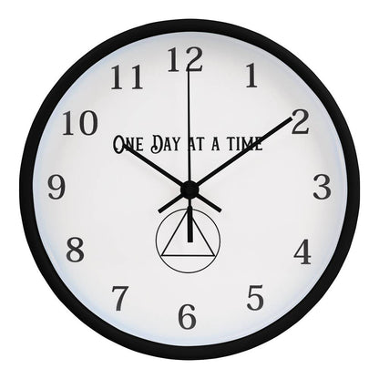 Close-up of a black round wall clock with “One Day At A Time” text and black hands