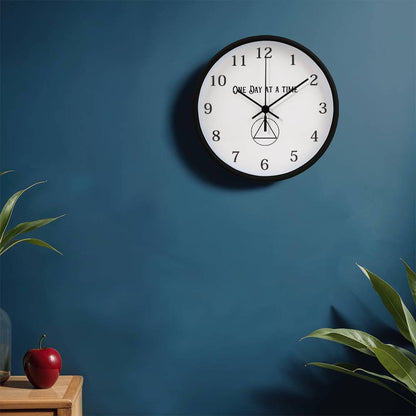 Black round wall clock with “One Day At A Time” text, black hour markers, and center icon