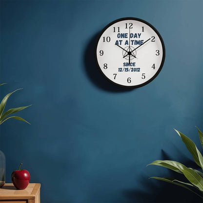 Wall clock with black rim and white face, 'ONE DAY AT A TIME' with compass-style center