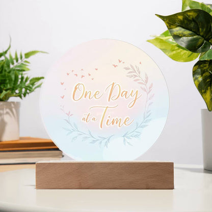 Round acrylic LED plaque with "One Day at a Time" text and floral wreath, wood base