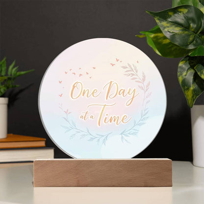 Round acrylic LED plaque with "One Day at a Time" floral design, on wood base