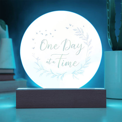 Illuminated round acrylic LED plaque with "One Day at a Time" floral accents, wood base