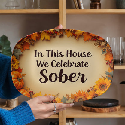 Oval serving platter on wooden stand with autumn leaf border and text "In This House We Celebrate Sober"