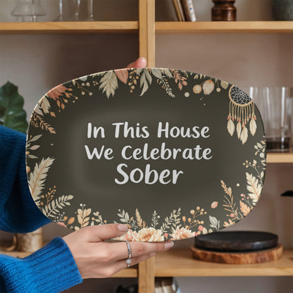Dark green oval serving platter held in hand with floral border and 'In This House' white text