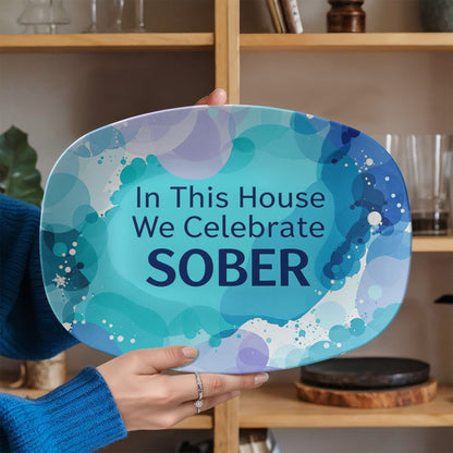 Oval serving platter close-up in hand, blue abstract design with 'In This House We Celebrate SOBER'.