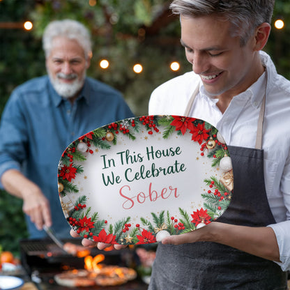 Oval serving platter with poinsettia wreath border held up, reading 'In This House We Celebrate Sober'