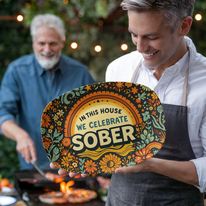 Decorative oval platter with “IN THIS HOUSE WE CELEBRATE SOBER” text held up