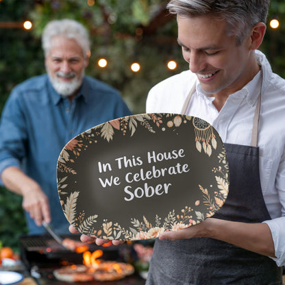 Dark green oval serving platter held outdoors with floral border and 'In This House...' text