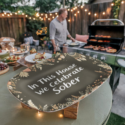 Dark green oval serving platter on wooden stand with floral border and white 'We Celebrate Sober'