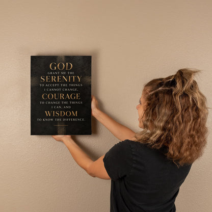 Black vertical canvas wall art with gold Serenity Prayer text, held against wall.