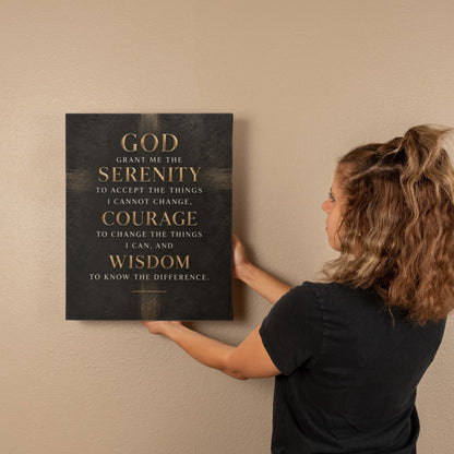 Black vertical canvas wall art with gold Serenity Prayer text, person adjusting placement.