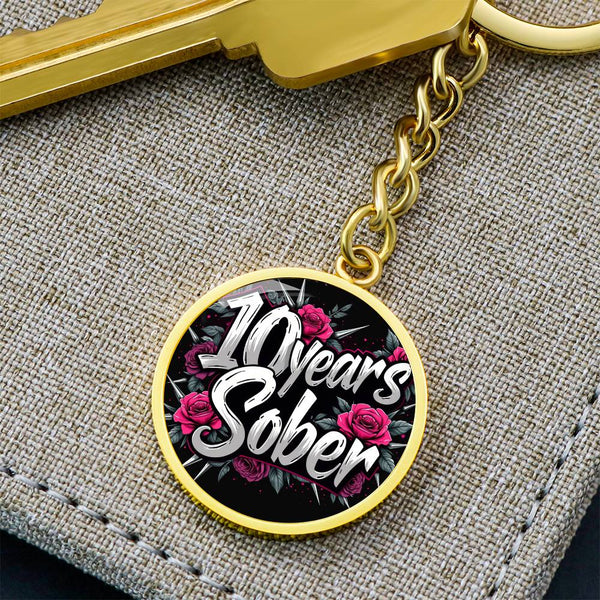 Gold round “10 Years Sober” keychain charm with pink roses on a chain