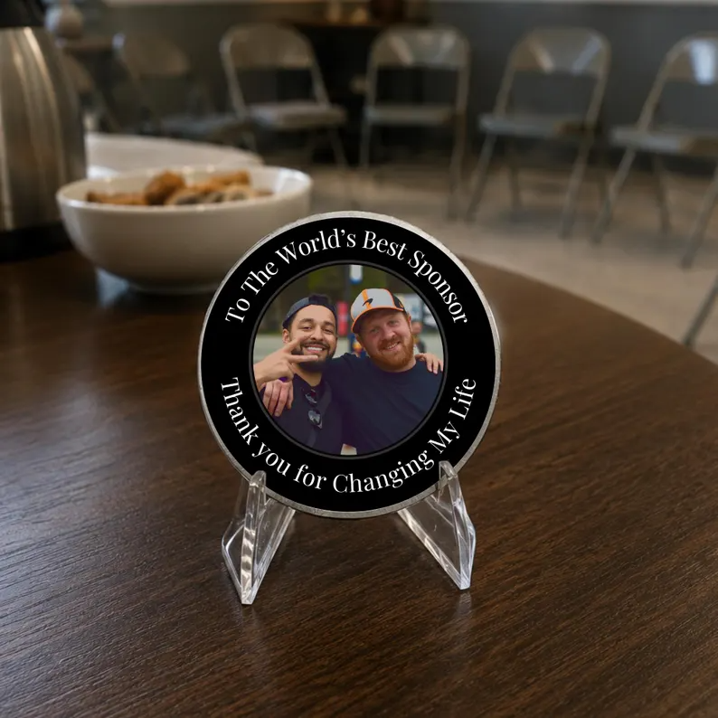 Round black photo coin with silver rim on a clear stand; features two smiling men.