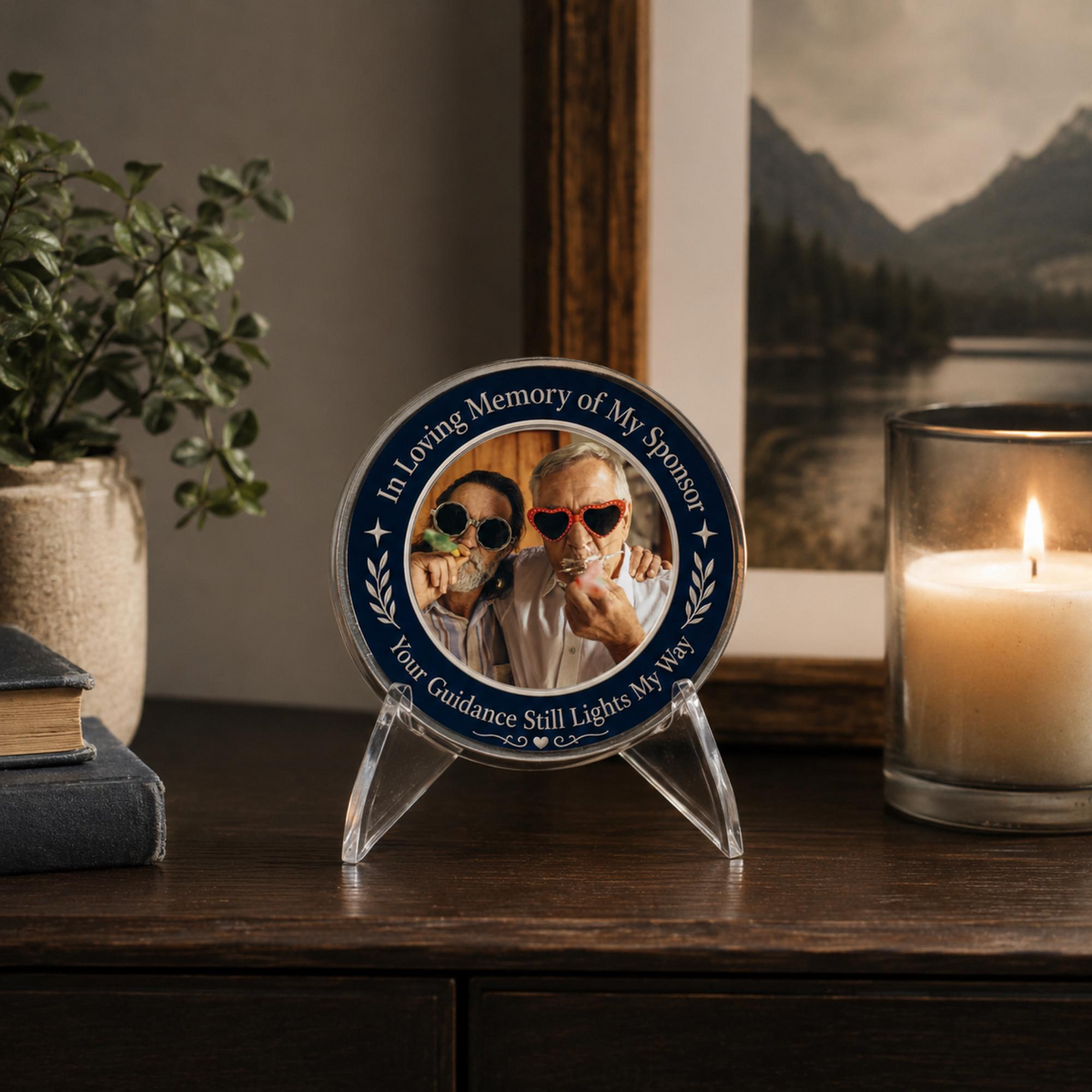 Blue memorial sponsor coin with two-photo portrait, on clear stand near a candle