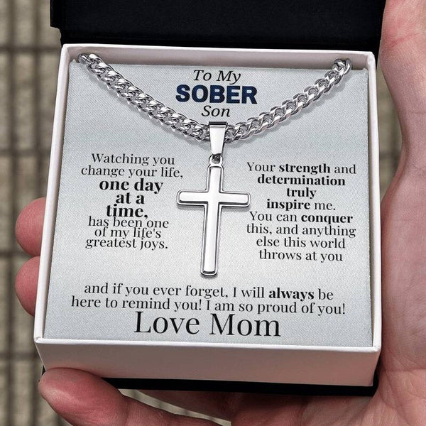 Silver cross pendant and curb-chain necklace inside white gift box tray.