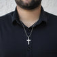 Silver cross pendant on ball-chain necklace worn with dark shirt