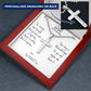 Silver cross necklace resting on engraved message card in red gift box