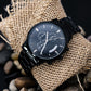 Black wristwatch with dark dial, three subdials, and black metal link bracelet